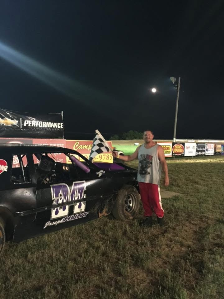 Joseph Hunt holding a checkered flag beside his dirt track race car